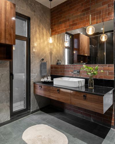 Floating wood vanity with vessel sink beneath exposed brick wall and pendant lights