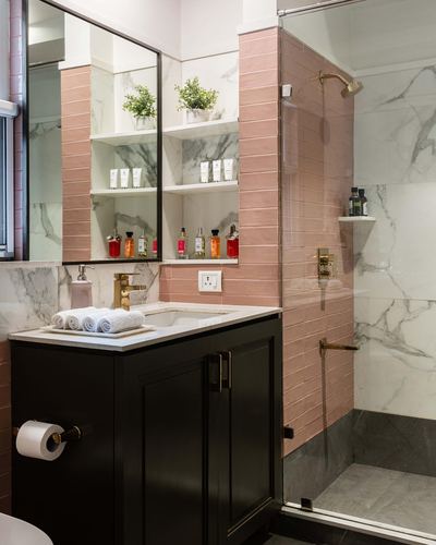 Bathroom vanity with black cabinet, pink tile wall, marble tile, brass fittings and glass shower.