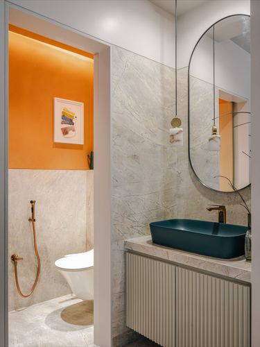 Stone-clad bathroom with teal vessel sink, oval mirror, and orange toilet room beyond