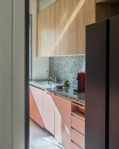 Kitchen view through doorway with pink cabinetry, wood-panel uppers, speckled stone counter, dark fridge