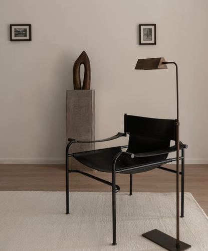 Black leather sling chair and bronze floor lamp beside a sculpture on a stone pedestal in a neutral room