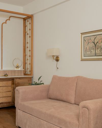 Blush sofa beneath brass sconce and framed art, beside a carved wooden arch niche