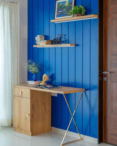 Blue vertical-paneled wall with floating shelves above a wooden desk with gold x-frame legs