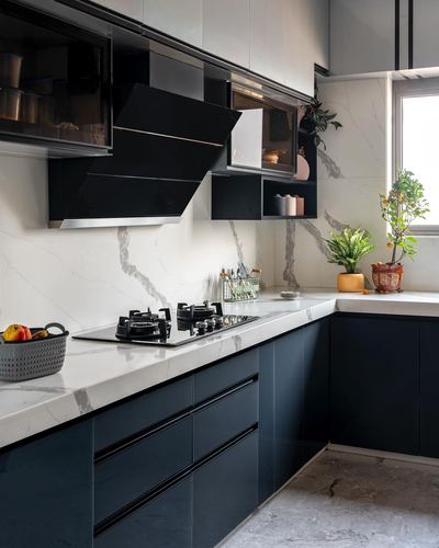 L-shaped kitchen with black cabinetry, veined stone counters and backsplash, angled chimney hood, window with plants