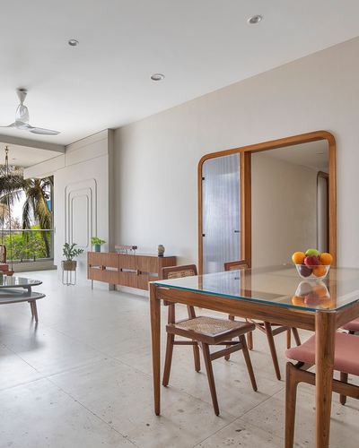 Dining area with glass-top wood table, cane chairs, and large arched mirror against balcony view