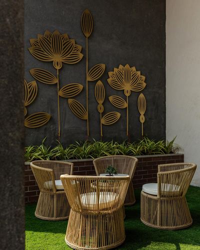 Cane chairs on artificial turf beneath a dark wall with gold lotus metal art and a planter.