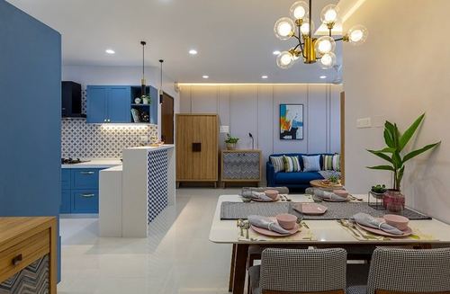 Open-plan apartment with blue kitchen, wood sideboard, dining table set for four, and blue sofa beyond