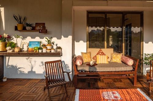 Sunlit balcony with wooden bench, patterned cushions, and plant-filled console table
