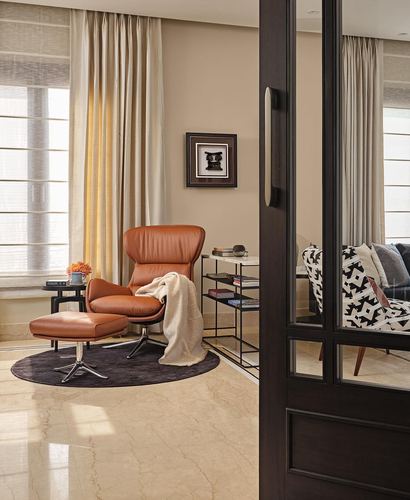 Rust leather recliner and ottoman on dark rug beside window in beige living room, seen through glass door.