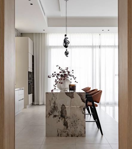 View through wooden doorway into kitchen with stone-clad island and sheer curtained window