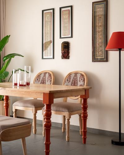 Dining table with cane-back chairs beneath framed scrolls and a red floor lamp