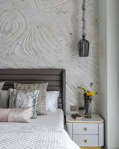 Bedroom corner with carved textured stone wall, brown leather headboard, and gold-trimmed nightstand with flowers
