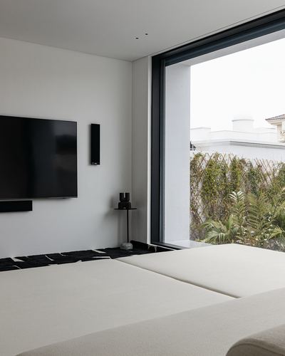 Minimalist bedroom corner with wall-mounted tv and full-height glass door opening to garden