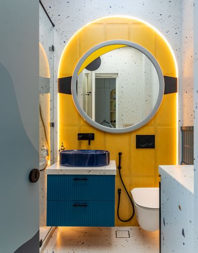 Bathroom with mustard tiled wall, backlit arched mirror, blue vessel basin and teal fluted vanity
