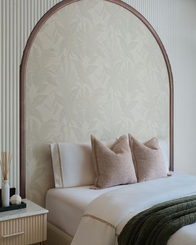 Arched bronze headboard with botanical wallpaper insert framing a white bed with blush pillows