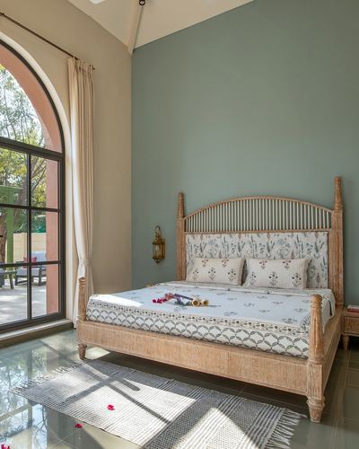 Bed with carved wooden four-poster frame against sage wall, arched door to garden
