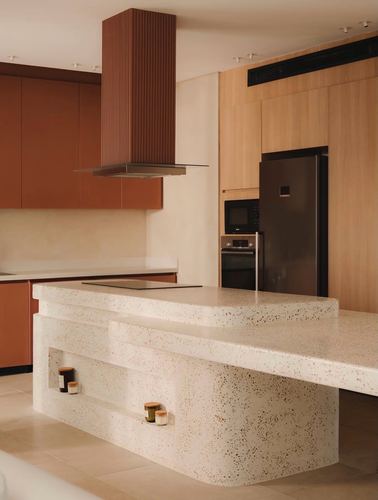 Terracotta and wood kitchen with sculpted terrazzo island and fluted extractor hood