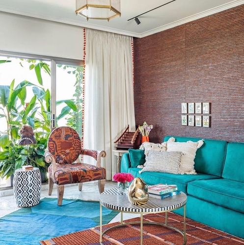 Living room with teal velvet sofa against textured rust wall, patterned armchair, and round striped coffee table
