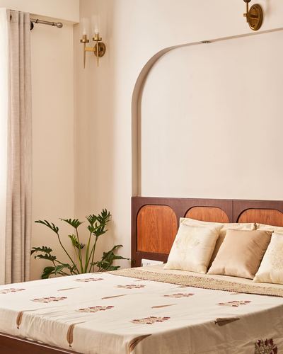 Bedroom with arched wall panel, wood headboard, brass sconces and cream embroidered bedding