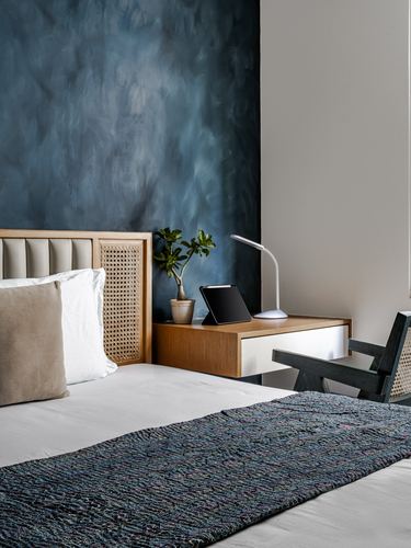 Bedroom corner with cane headboard, blue textured wall, floating wood nightstand and lamp