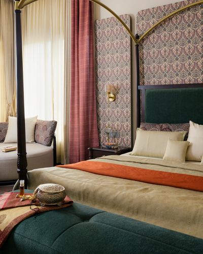 Bedroom with brass canopy bed, green velvet headboard, patterned wall panels and pink curtains