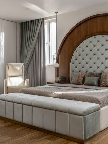 Bedroom with arched wood wall, tufted headboard, storage bench, and sage curtains