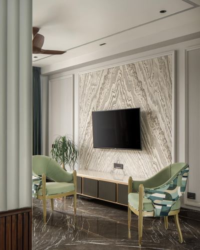 Living room with book-matched stone accent wall, mounted tv, gold-framed console, and green velvet chairs on either side