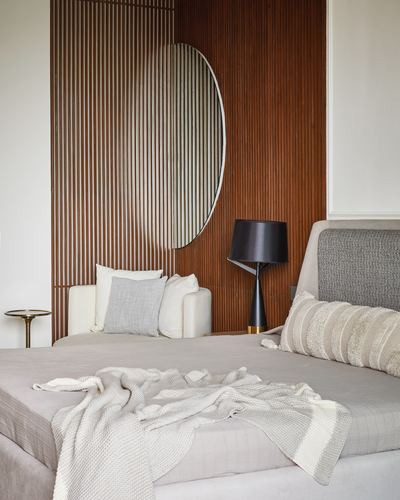 Bedroom with slatted wood wall, round mirror, black lamp, and neutral bedding.