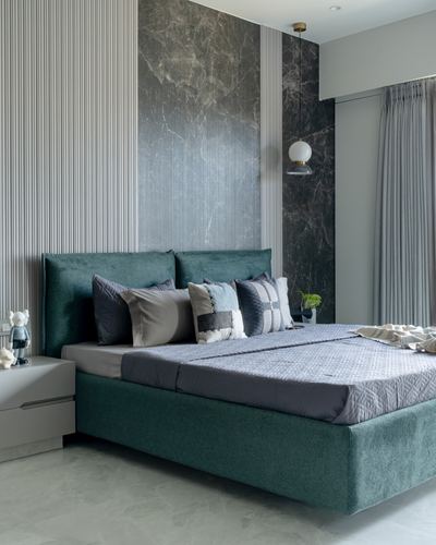 Teal upholstered bed against dark stone-textured wall with globe pendant light and striped wallpaper