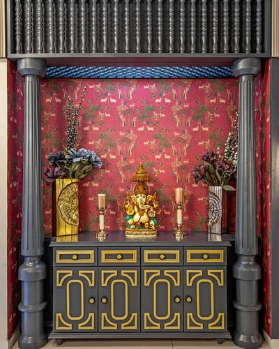 Pooja unit with charcoal cabinet, gold trim, turned pillars, and printed maroon wallpaper backdrop