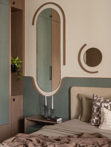 Bedroom corner with arched wooden mirror, round mirror, wardrobe and upholstered headboard against sage wall