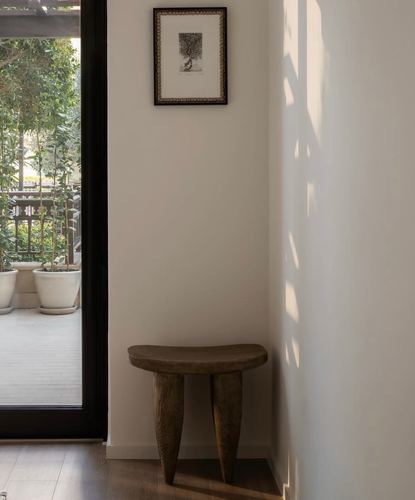 Wooden Senufo-style stool in a sunlit corner beside a framed print and glass door to garden