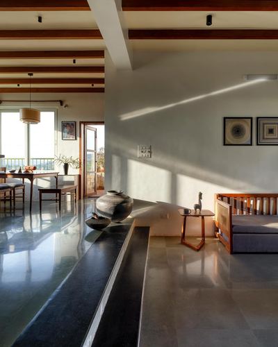 Sunlit living room with exposed wood beams, stone flooring, black pot and cane-backed sofa