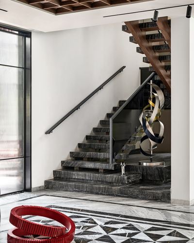 Floating stone staircase with wood underside above a geometric marble foyer floor and metal sculptures