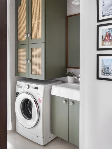 Sage green cane-front cabinets above a washing machine beside a white sink in a utility bathroom