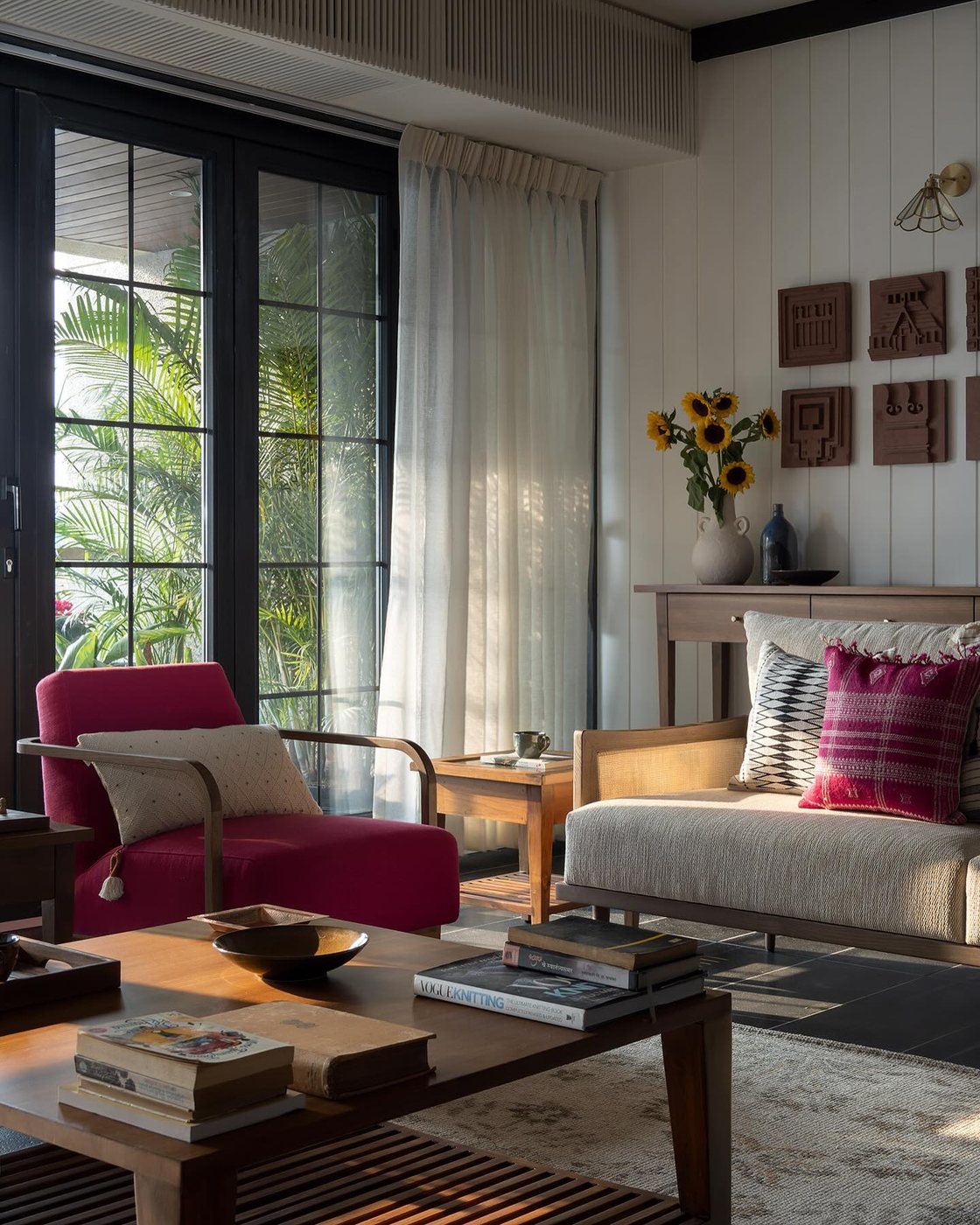 Living room with magenta armchair, wooden sofa, and terracotta wall tiles beside glass doors