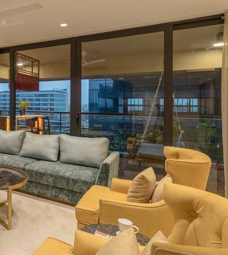 Living room with green velvet sofa and mustard armchairs facing floor-to-ceiling windows overlooking city skyline