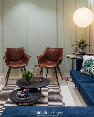 Two brown leather armchairs and navy sofa around round black coffee tables under a globe pendant light