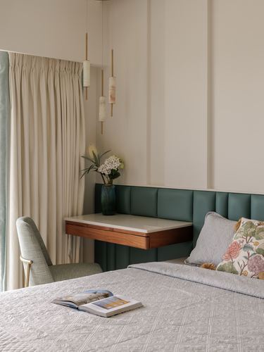 Bedroom corner with green tufted headboard, floating wood nightstand, and hanging pendant lights