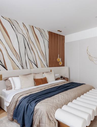 Bedroom with patterned wallpaper headboard wall, wood panel accent, pendant lights, and tufted bench at foot of bed