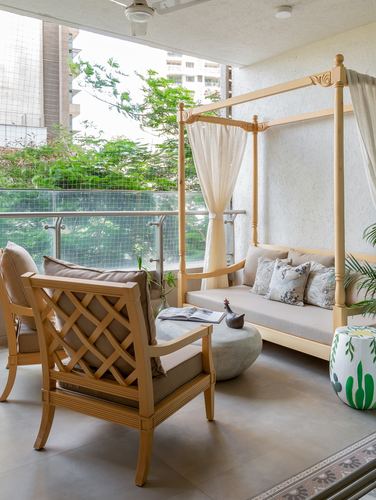Balcony seating with wooden canopy daybed, lattice armchairs, and stone side table facing greenery