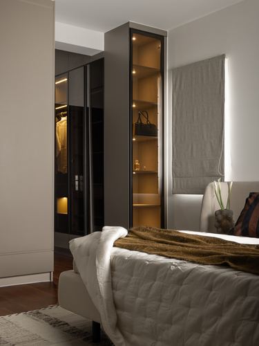 Bedroom corner with backlit glass display cabinet beside mirrored wardrobe and bed with fur throw