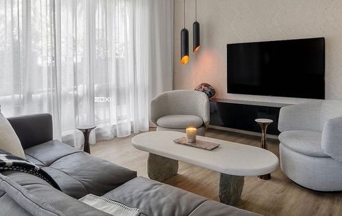 Neutral toned living room with curved sofa, cream armchairs, oval stone coffee table and wall-mounted tv