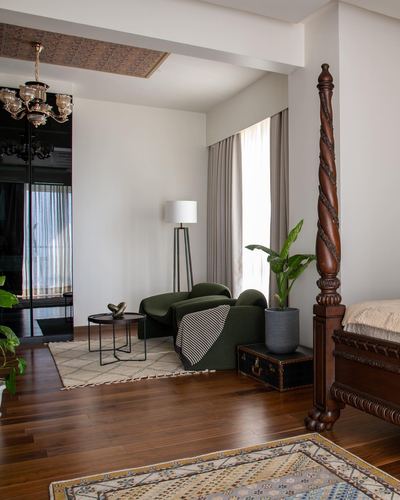 Bedroom corner with carved four-poster bed, green armchair, and wood flooring