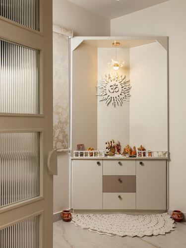 Small pooja unit with om wall carving, pendant light, deity idols on cabinet, fluted glass door beside
