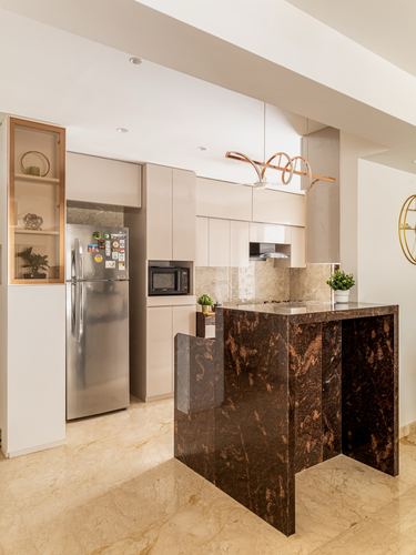 Beige kitchen with stainless fridge, glossy cabinets, and a dark stone island with sculptural pendant light