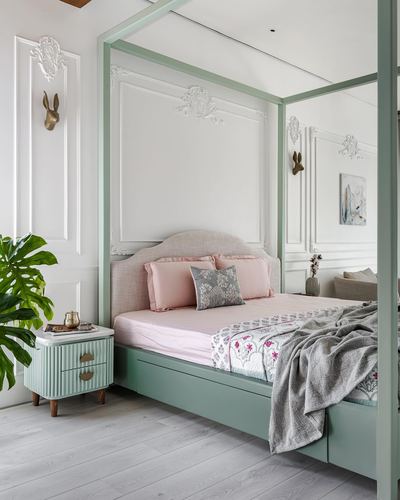 Sage-green four-poster bed with pink bedding against white moulded wall panels in a Pune bedroom