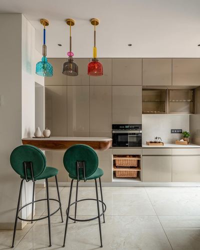 Kitchen counter with blue, grey and red glass pendant lights over green velvet bar stools