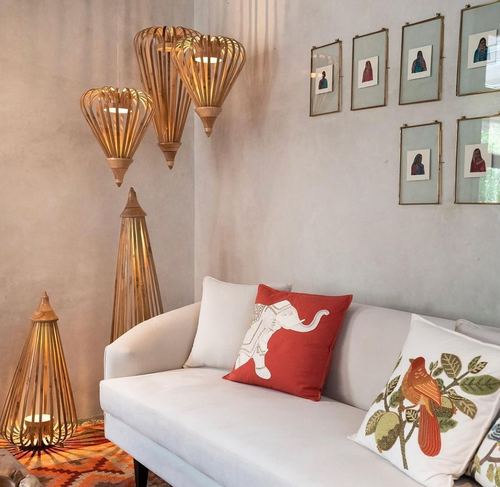 Cream sofa with elephant and bird cushions beside woven wooden lanterns and framed portrait prints on textured wall