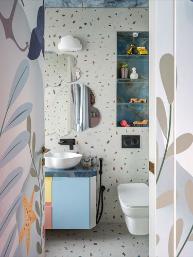 Playful terrazzo-walled bathroom with cloud mirror, blue vanity, and glass shelf displaying toys